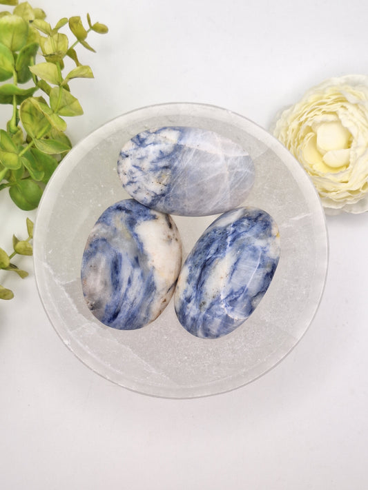 A collection of polished Afghanite palm stones with vibrant blue and white patterns. A rare mineral related to Sodalite, valued for both its geological beauty and metaphysical properties