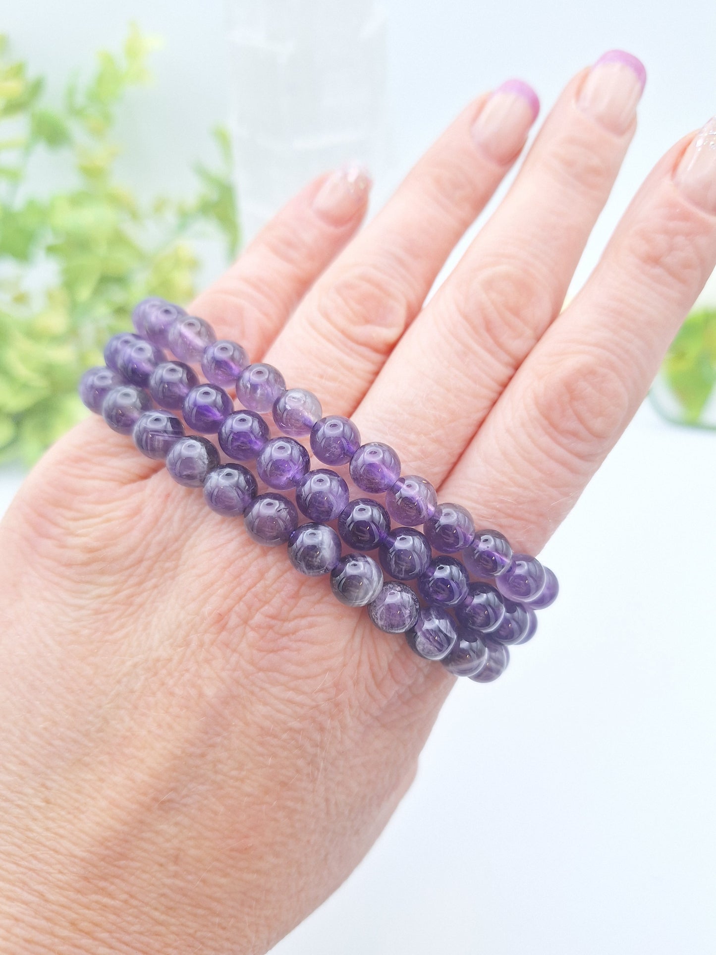 Three Amethyst 8mm beaded bracelets wrapped around four fingers, highlighting their deep purple color and smooth, polished beads.