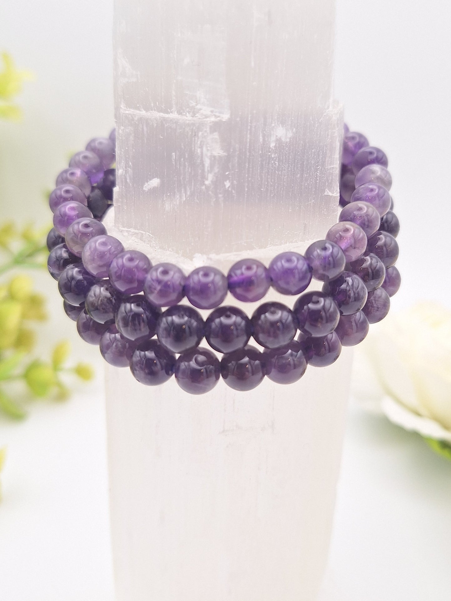 Three Amethyst 8mm beaded bracelets resting on a selenite tower, displaying their rich purple color and translucent quality.