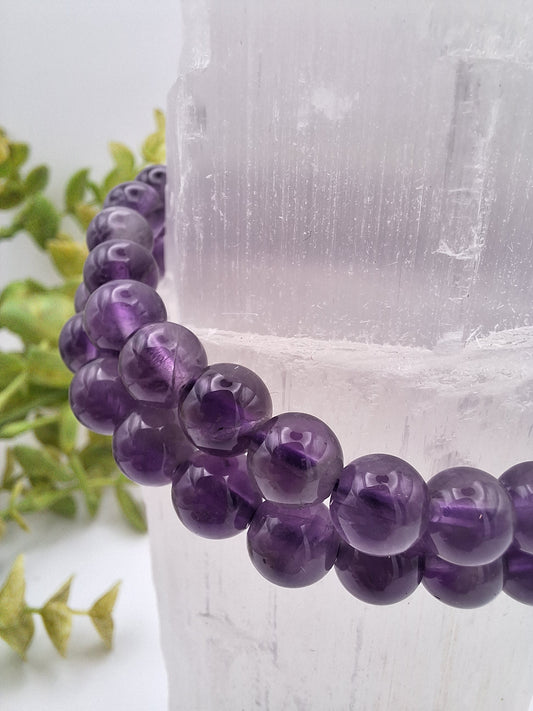 Close-up of two Amethyst 8mm beaded bracelets draped over a selenite tower, showcasing their deep purple hue and smooth, polished beads.