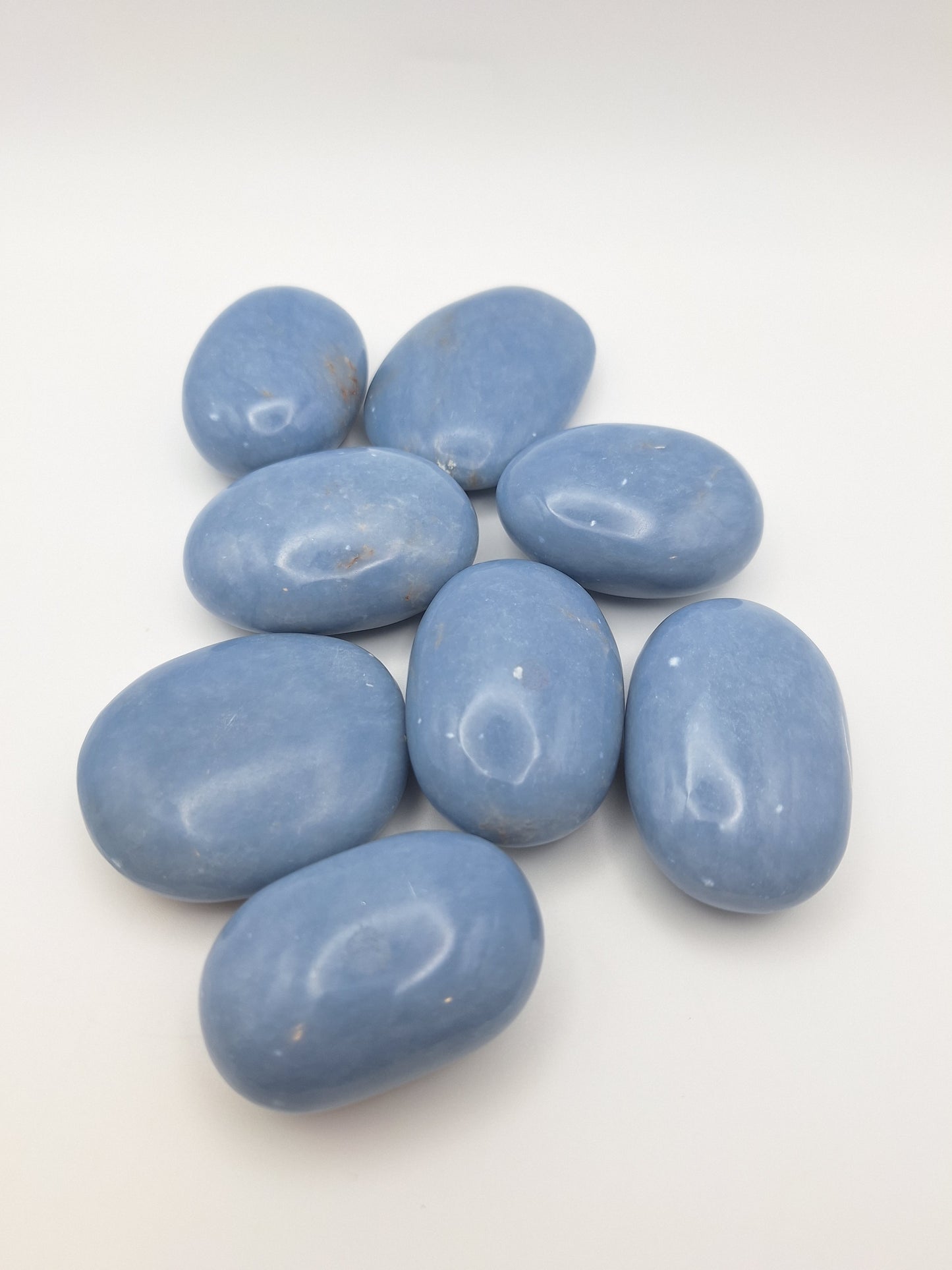 A group of eight Angelite palm stones, all polished smooth with a soft blue hue, known for their peaceful and spiritual properties.