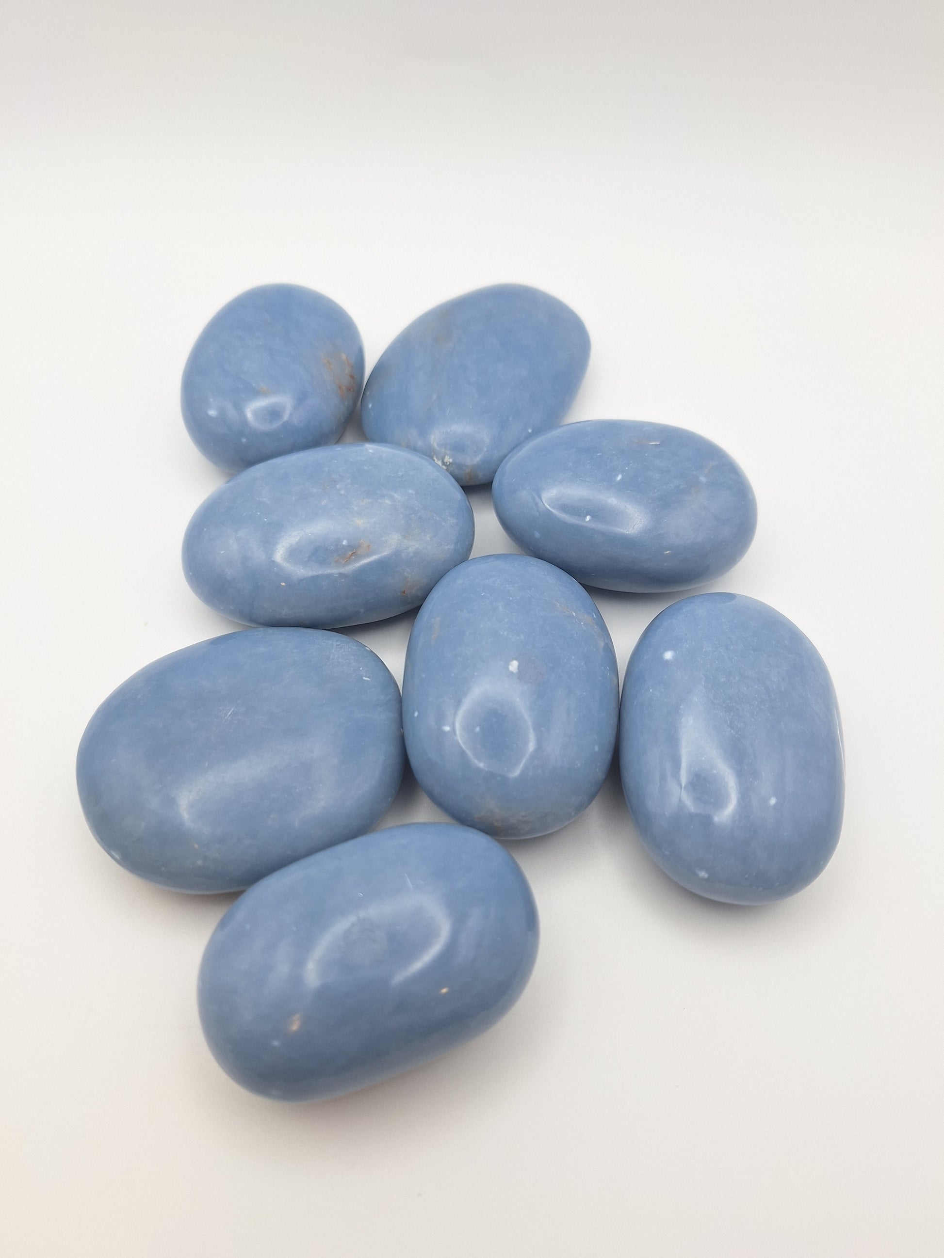 A group of eight Angelite palm stones, all polished smooth with a soft blue hue, known for their peaceful and spiritual properties.
