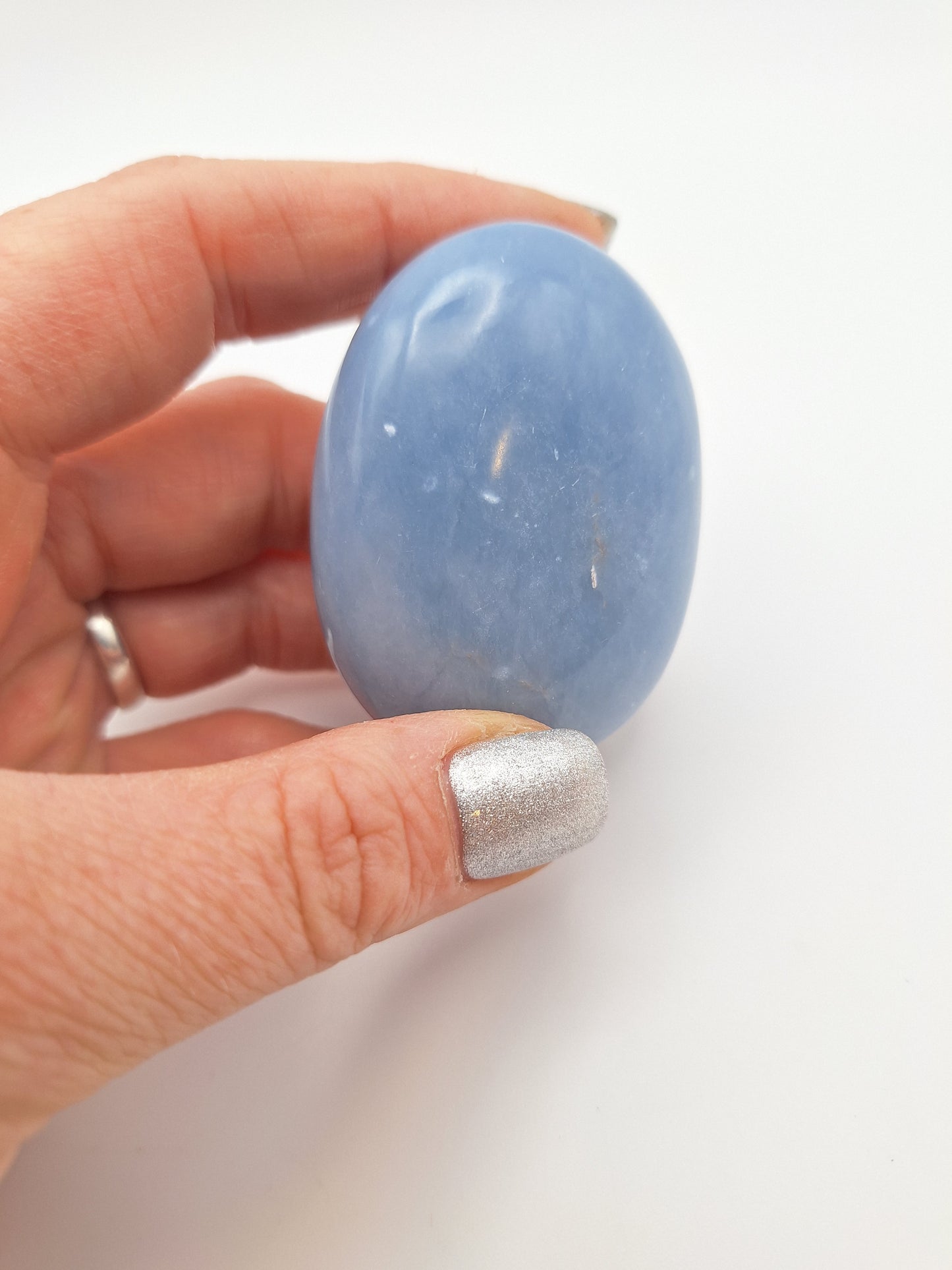 A hand holding a polished Angelite palm stone, showcasing its smooth, powder-blue surface and calming energy.