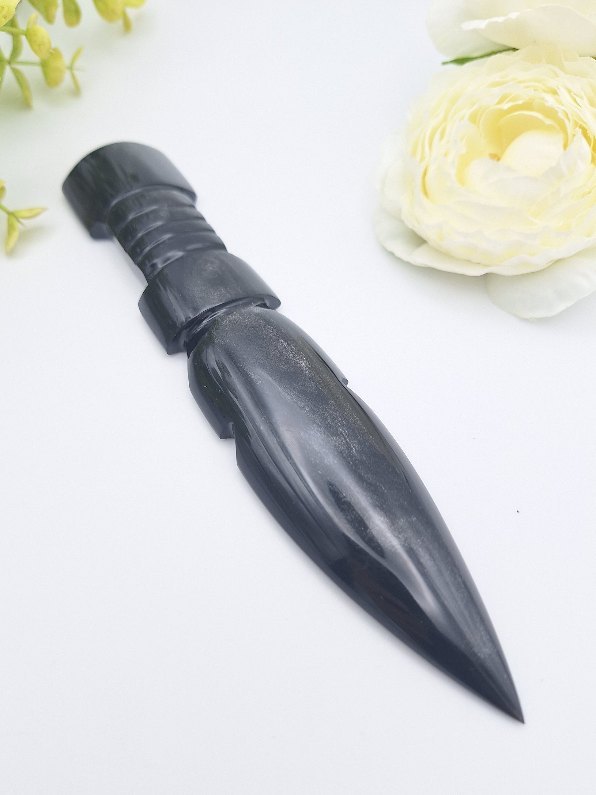 Black Obsidian carved dagger displayed at a left angle with a delicate flower, highlighting its polished blade and smooth handle.