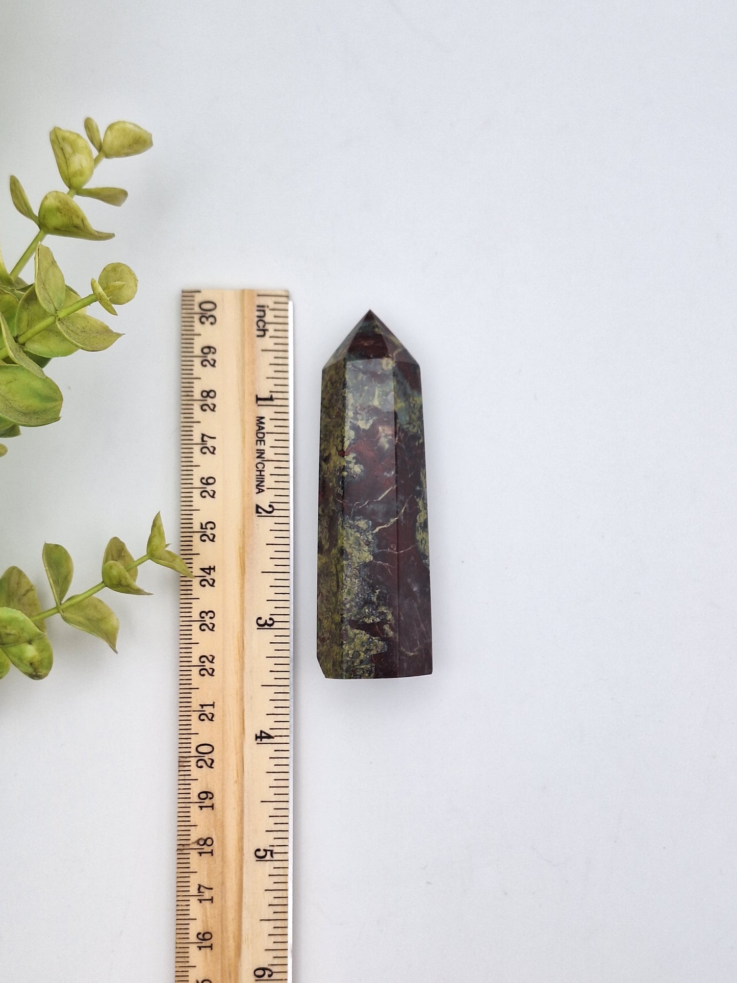 Dragon Bloodstone tower placed next to a ruler for size reference. A natural combination of Epidote and Piemontite, known for its grounding and energizing properties.