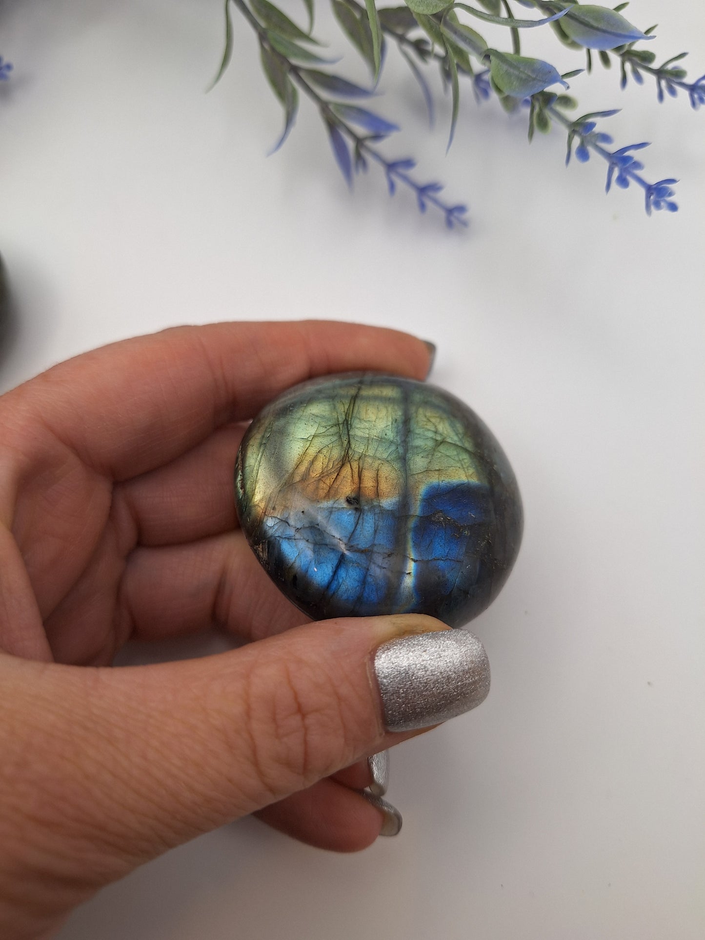 A hand holding a polished Labradorite palm stone, revealing its vibrant flash of blue and gold under the light.