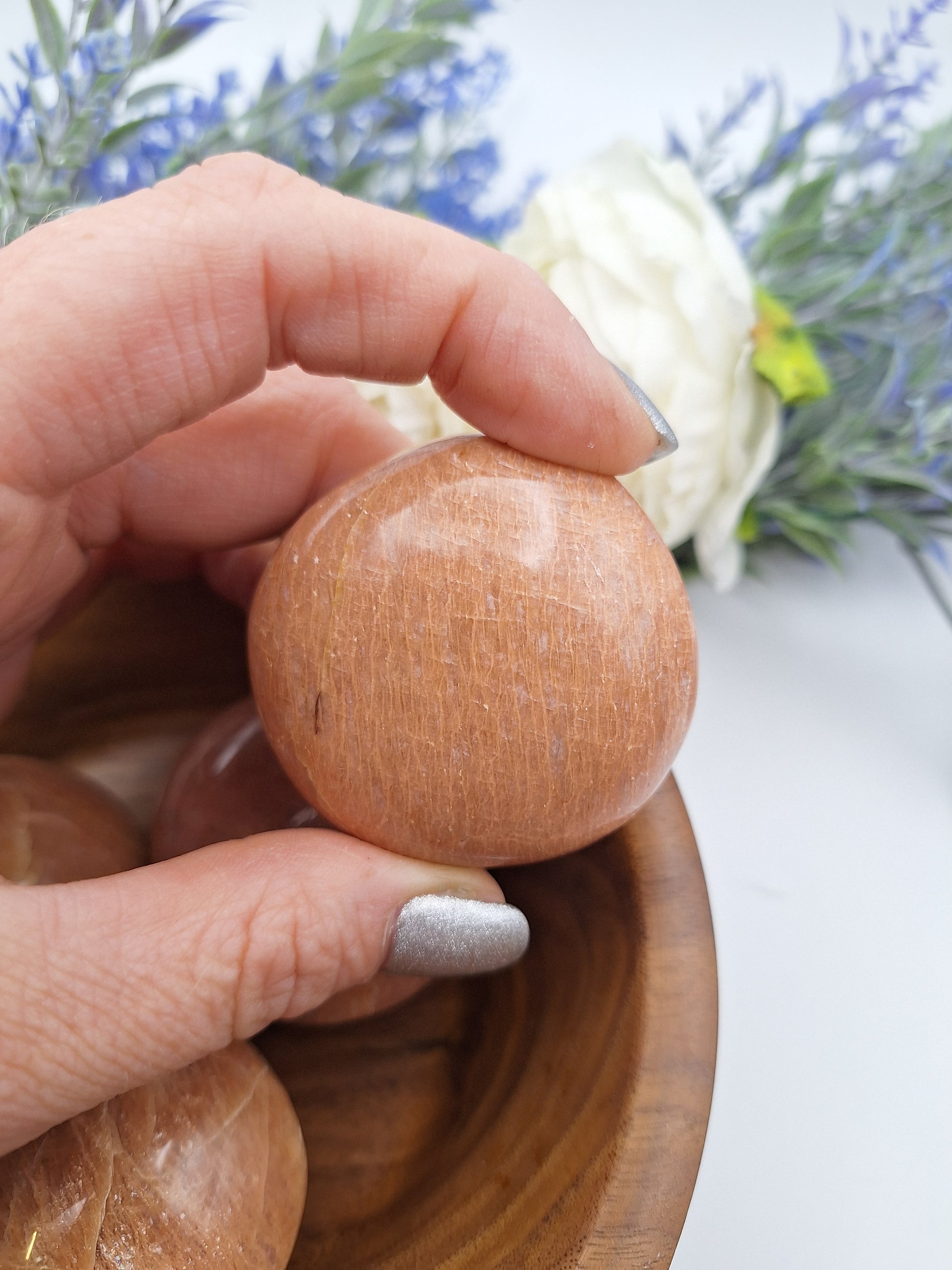 A smooth, polished Peach Moonstone palm stone resting in a hand, showcasing its soft peach tones and natural shimmer.