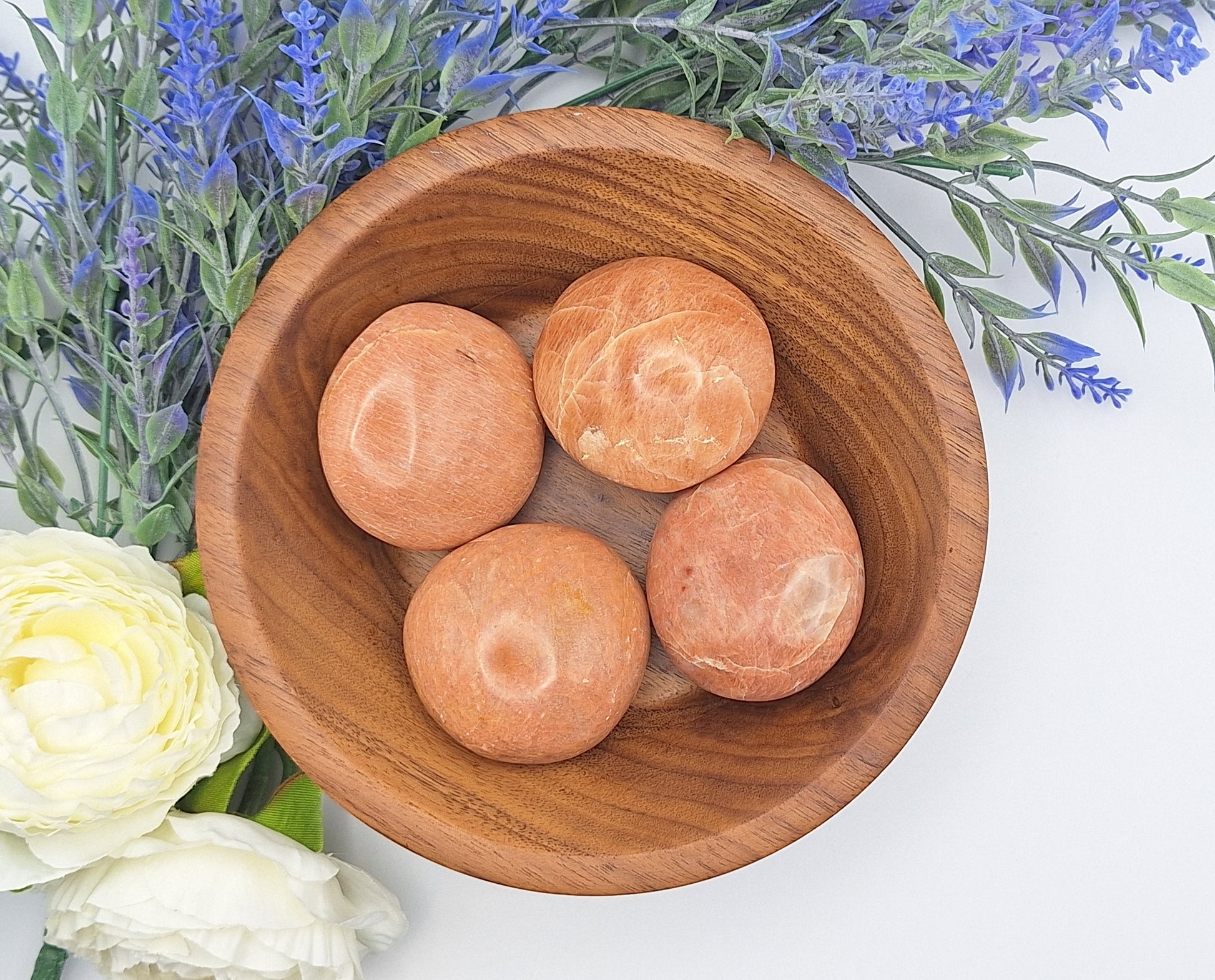 A wooden bowl filled with polished Peach Moonstone palm stones from Madagascar, displaying soft peach and cream hues with a gentle shimmer.