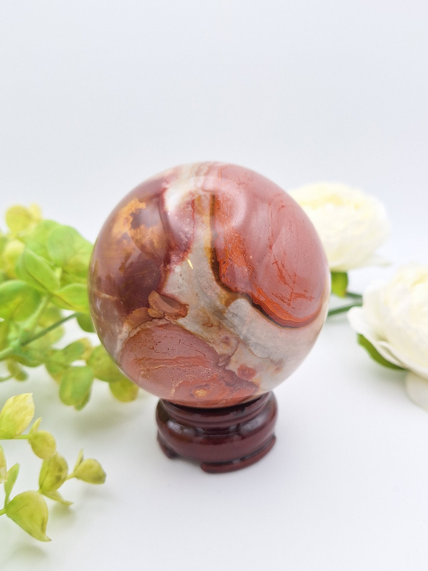 Polished Polychrome Jasper sphere resting on a stand, showcasing its warm earth tones and swirling patterns.