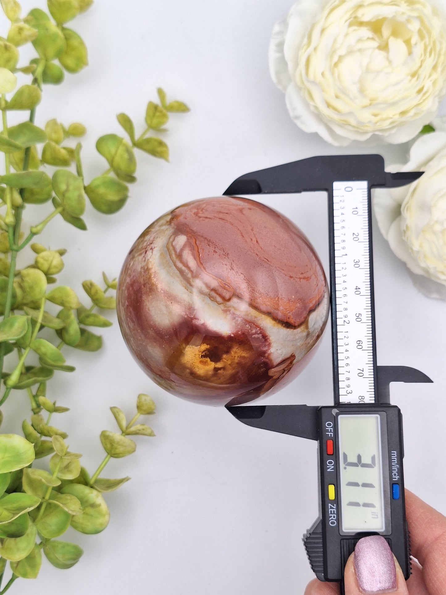 Polychrome Jasper sphere measured with calipers for size reference, showing its smooth polish and natural patterns.