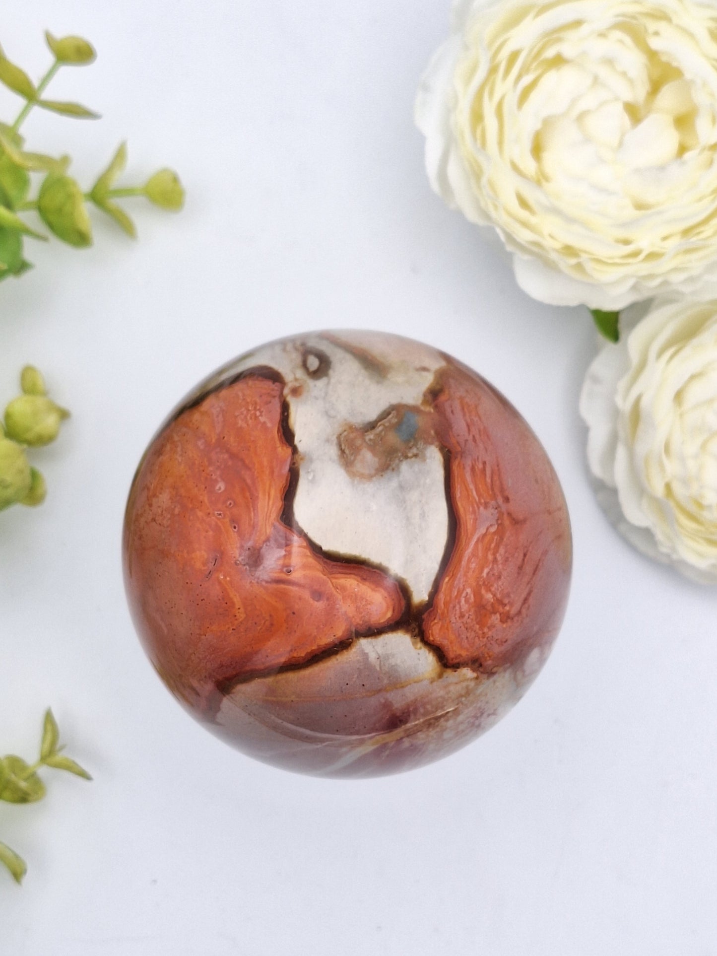 Top-down view of a Polychrome Jasper sphere, showcasing its unique swirls of red, orange, and cream hues.