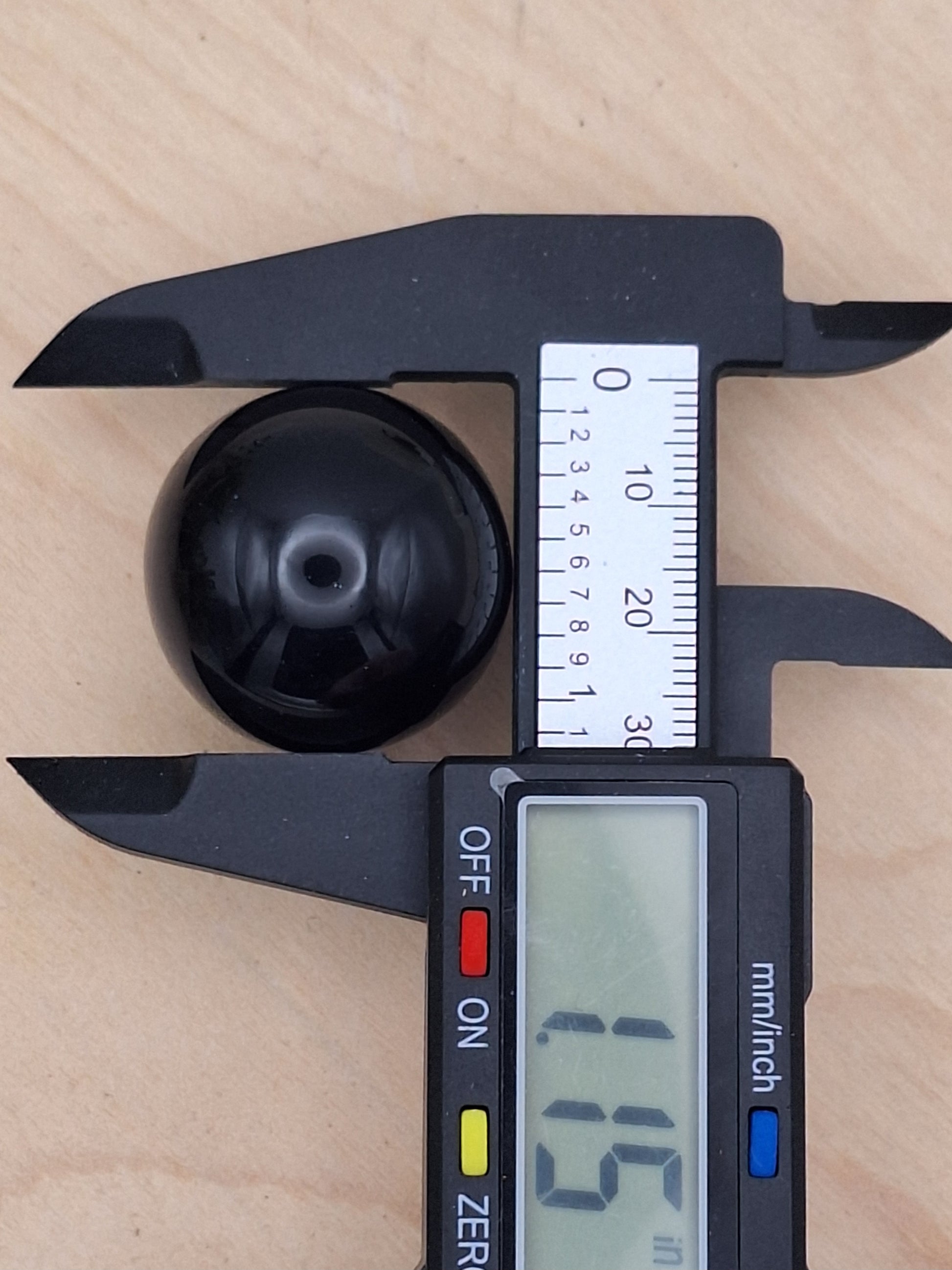 Black obsidian sphere in a caliper measuring tool with 1.15 inches showing on the digital display for a size reference.