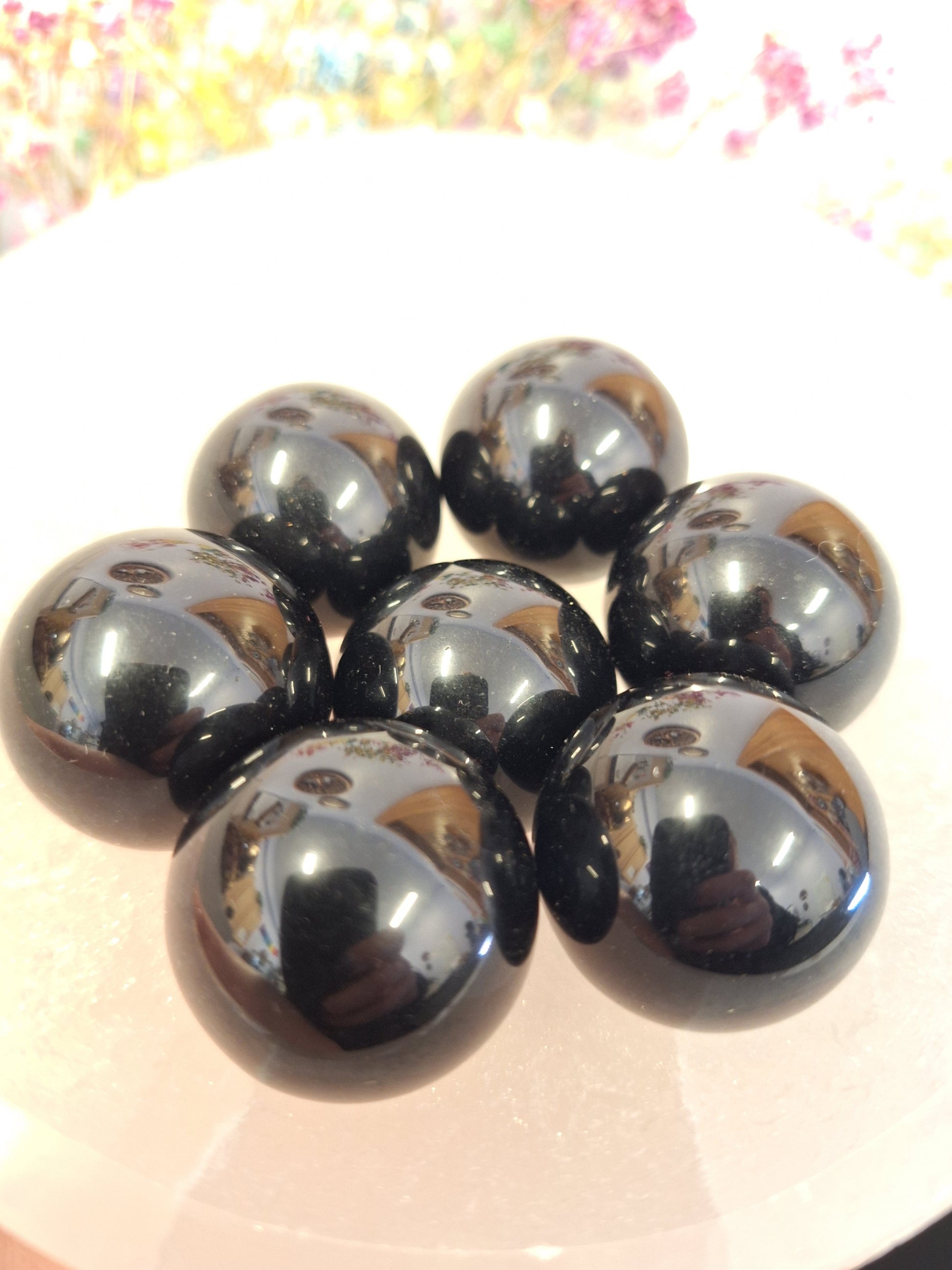 A close up shot of a group of small shiny black obsidian polished spheres in a white bowl.