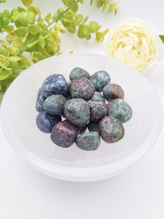 A wooden bowl filled with polished Ruby Kyanite tumbled stones from India, showcasing deep blue Kyanite with embedded Ruby inclusions.