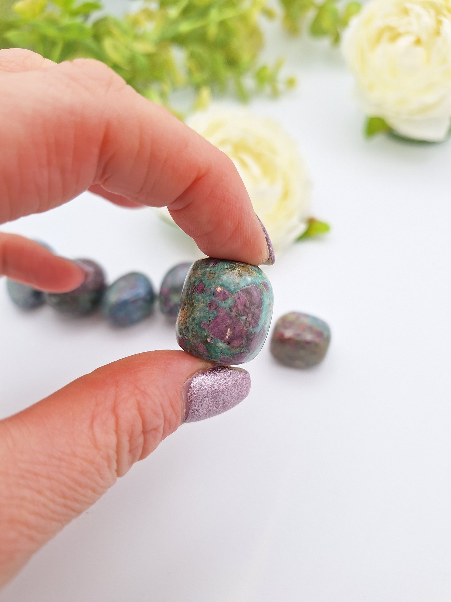A hand holding a polished Ruby Kyanite tumbled stone, highlighting its mix of deep blue Kyanite and embedded Ruby inclusions.