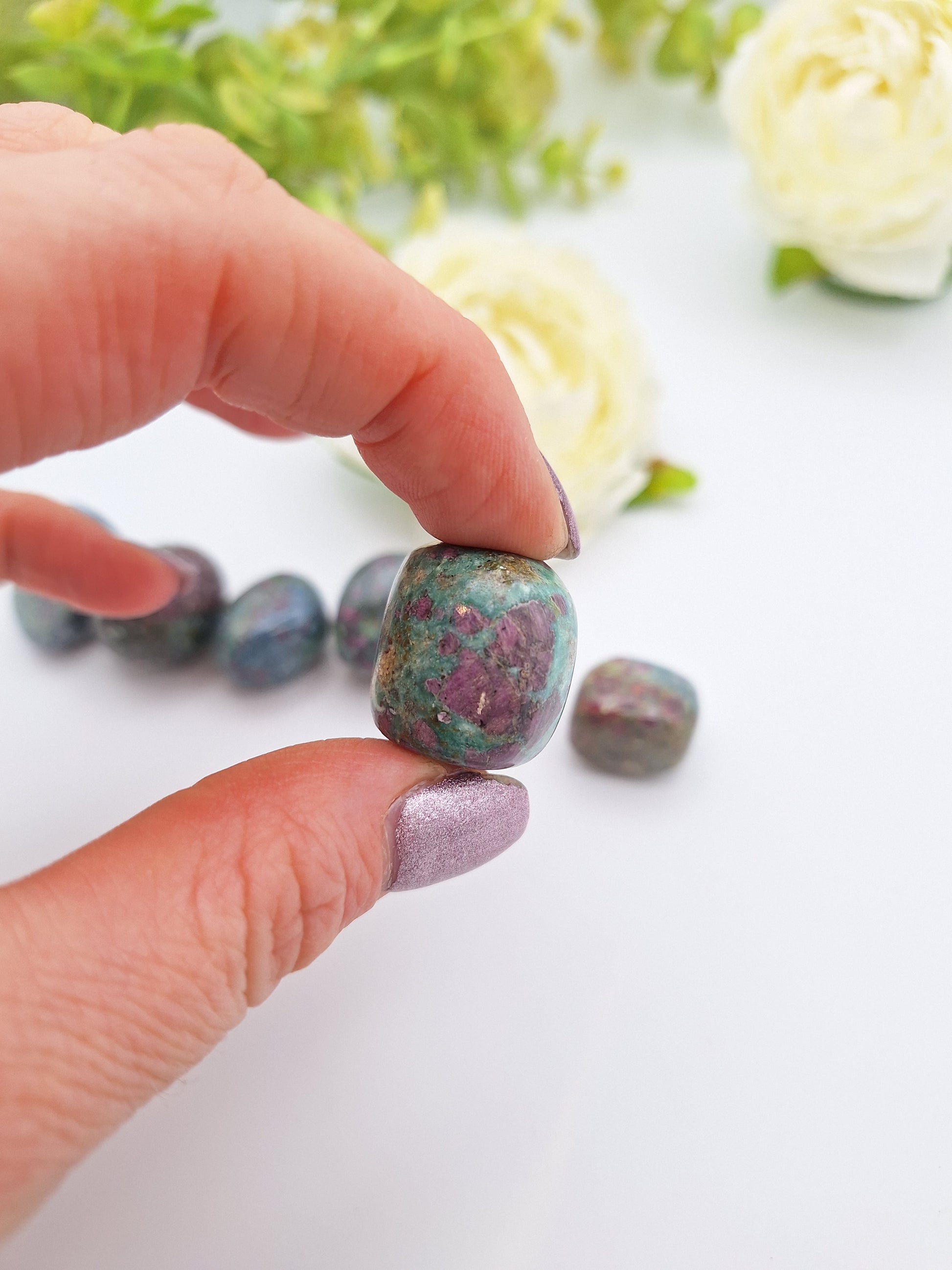 A hand holding a polished Ruby Kyanite tumbled stone, highlighting its mix of deep blue Kyanite and embedded Ruby inclusions.