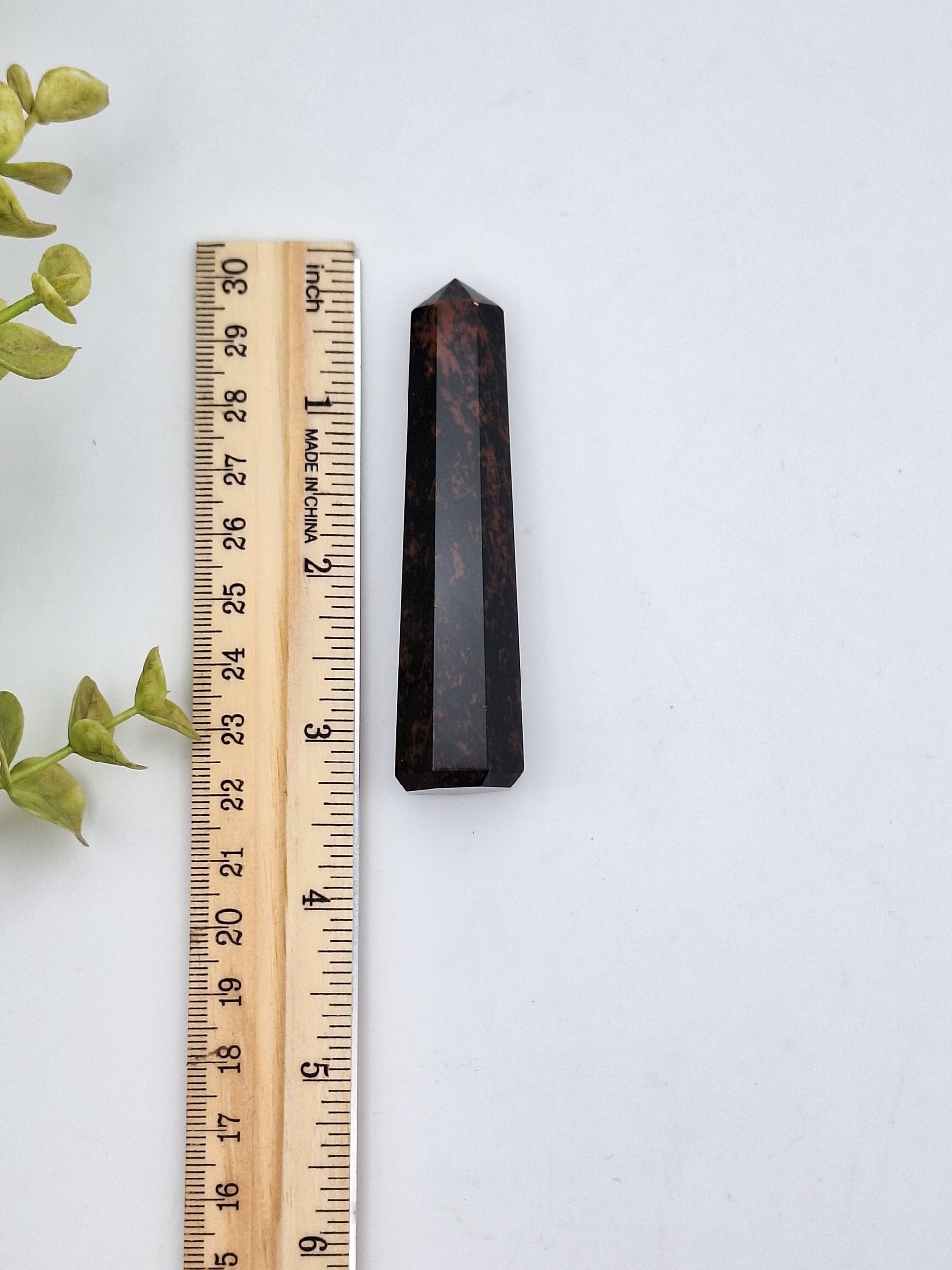 A Mahogany Obsidian tower point placed next to a ruler for size reference, showing its polished surface and unique color variations.
