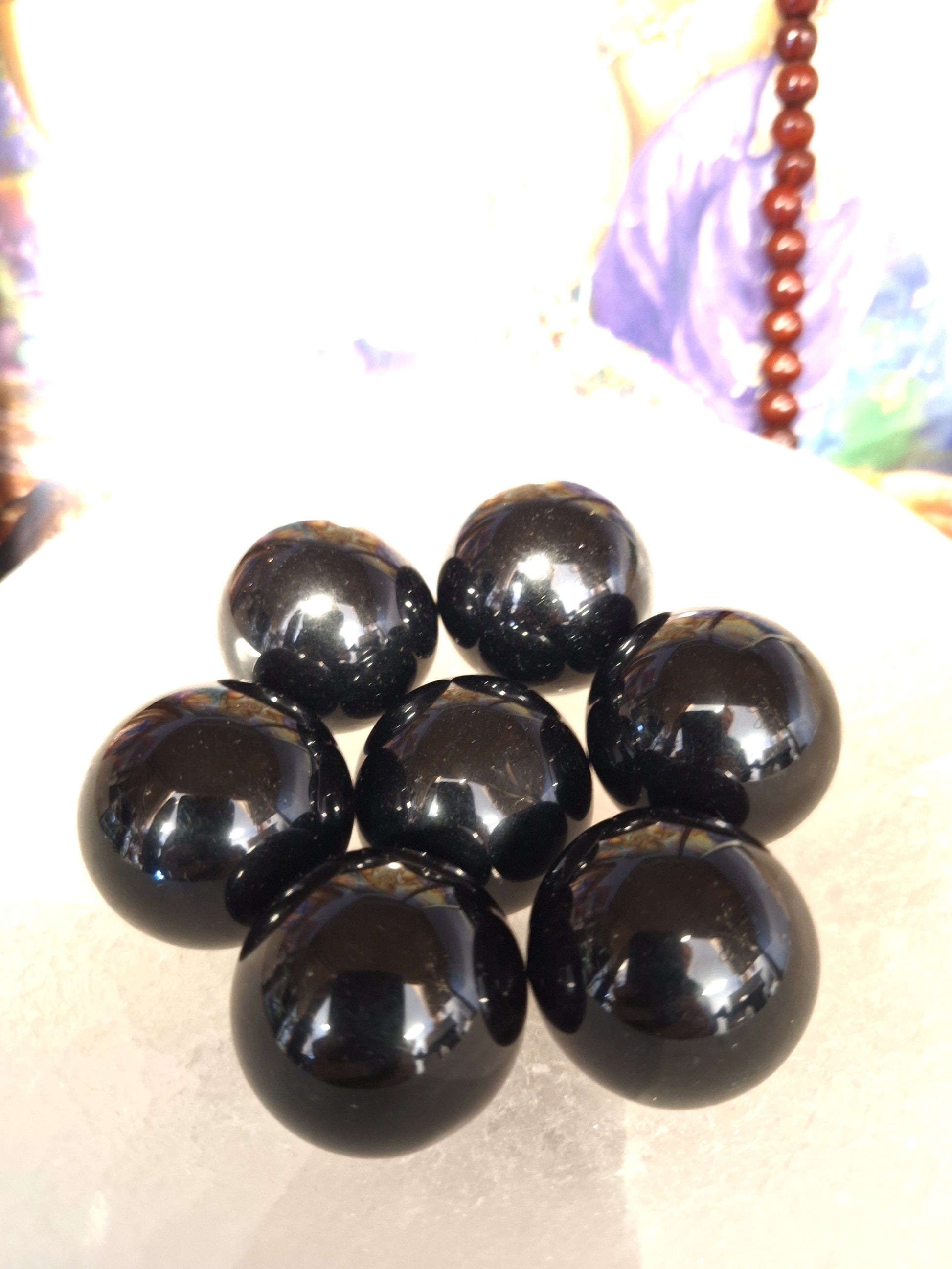 Seven black obsidian spheres in a black bowl, showcasing a shiny reflective finish. 
